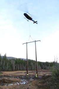 A fully framed composite utility structure is being transported by a small helicopter by air